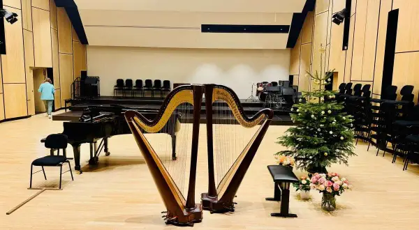 Ein festlich geschmückter Weihnachtsbaum steht neben einer Harfe, die für den Aufbau bereitsteht. Ein Flügel und Stühle sind ebenfalls zu sehen.