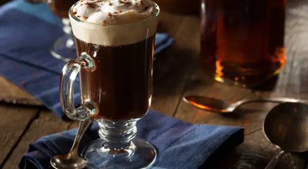 En värmande irish coffee med vispad grädde och kanel på en blå duk.