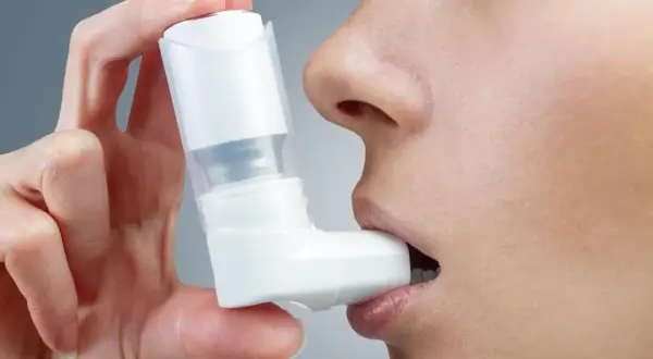Dłoń trzymająca inhalator przy ustach osoby.