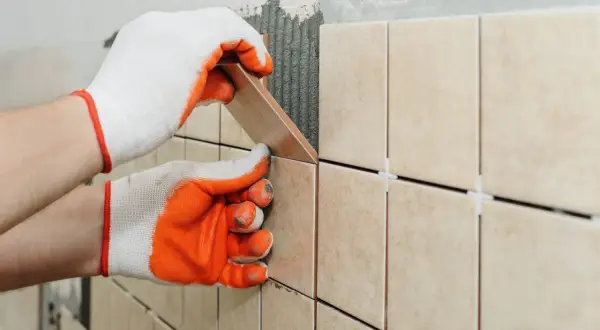 Hands in gloves carefully place a tile, demonstrating how to tile a shower floor.