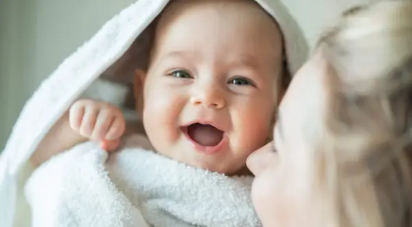 La alegría contagiosa cuando empieza a reírse un bebé, envuelto en una toalla blanca, con una madre dándole un beso.