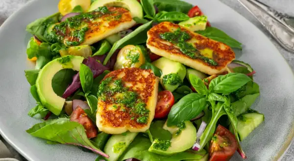 Pyszna sałatka z halloumi, awokado, pomidorkami i ogórkiem, polana zielonym sosem.