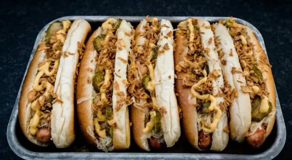 Sechs Hot Dogs in einem Blech, belegt mit Gurken, Sauerkraut, Senf und knusprigen Zwiebeln – die perfekten Hot Dog Zutaten für jeden Geschmack.