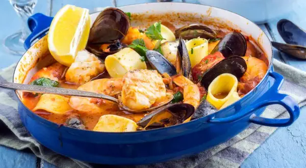 Caldereta de pescado humeante en cazuela azul, con gambas, mejillones, trozos de pescado blanco y limón.