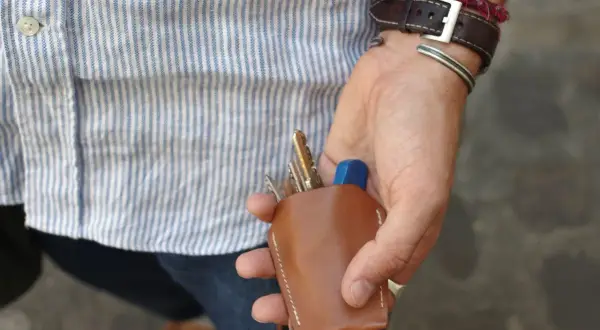 Main d'un homme au style workwear, tenant un étui à clés en cuir marron.