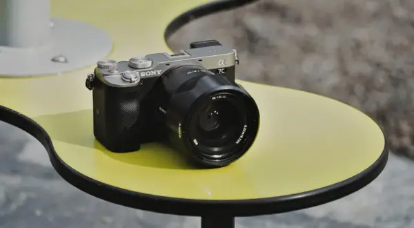 Srebrno-czarny aparat Sony a7c z obiektywem na żółtym stoliku.