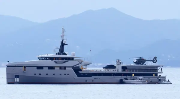 Lo yacht Koru, con il suo elicottero pronto al decollo, naviga maestoso in acque tranquille, con le montagne sullo sfondo.