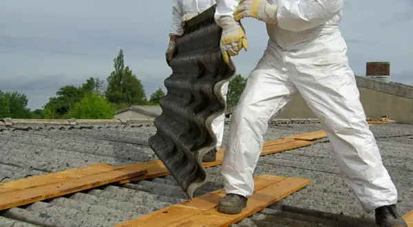 Arbeiter in Schutzanzügen entfernen eine Wellplatte. Bis in die 1990er Jahre wurde Asbest verbaut.