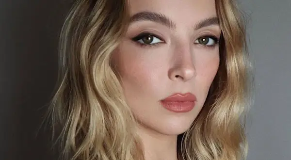 Kobieta z falowanymi, blond włosami, które wyglądają jak po karbowaniu. Delikatny makijaż podkreśla jej urodę.