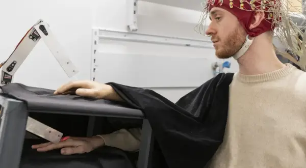 Joel Svenningsson med EEG-hjälm och en robotarm som interagerar med hans hand.