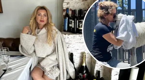 Eva Halina Rich w swetrze siedzi przy stole, a obok niej wesoło przytula białego zwierzaka.