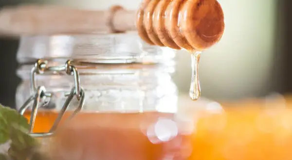Ein Holzlöffel tropft goldenen Akazienhonig in ein Glas. Dieser Honig ist nicht nur süß, sondern auch gesund.