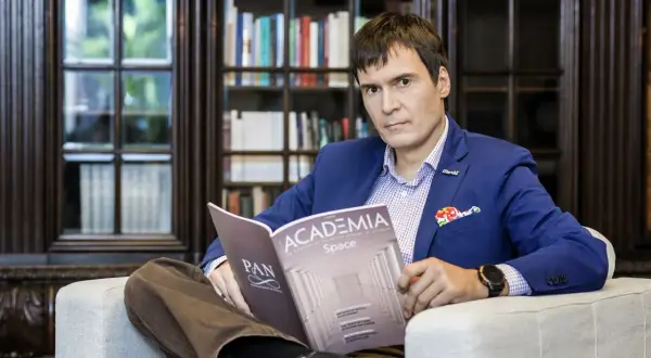 Mężczyzna w niebieskiej marynarce siedzi w fotelu i czyta czasopismo "Academia".