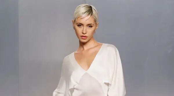 Iris Law, con su corte de pelo rubio platino y un elegante vestido blanco, posa con una mirada cautivadora.