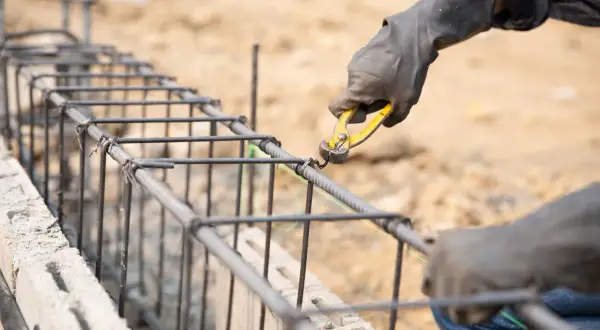 Manos enguantadas atando varillas de acero para como hacer los cimientos de una casa.