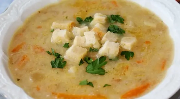 Aksamitna zupa cebulowa z grzankami i natką pietruszki, podana w białej misce.