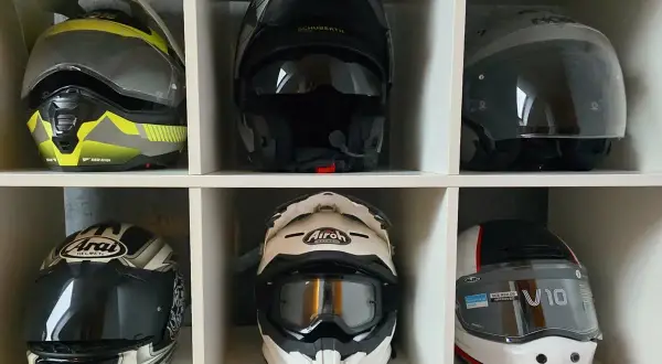 Sześć kasków motocyklowych różnych marek i stylów, ułożonych w białych przegrodach.