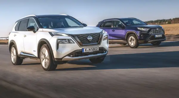 Biały Nissan X-Trail i fioletowy SUV jadą po drodze.