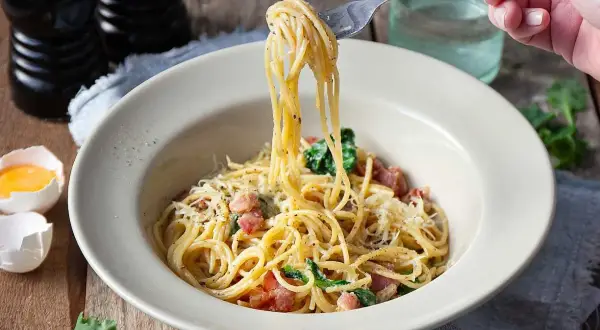 En gaffel lyfter en portion krämig spaghetti carbonara från en skål. Ett perfekt pasta carbonara recept för en god middag.