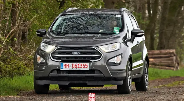 Szary Ford Ecosport na leśnej drodze. Kierowca w okularach za kierownicą.