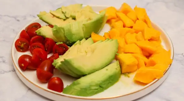 Plato con ensalada de mango y aguacate, tomates cherry cortados por la mitad y aguacate en láminas.