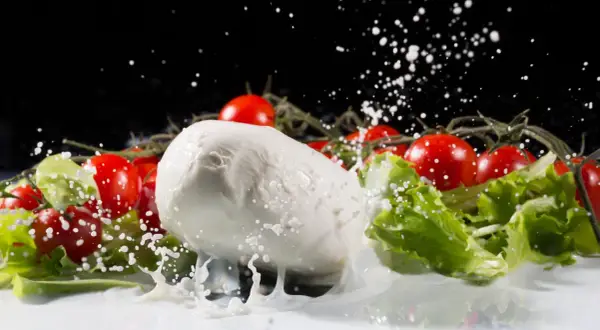 La mozzarella fresca, circondata da pomodorini e lattuga, viene spruzzata con latte in un movimento dinamico.