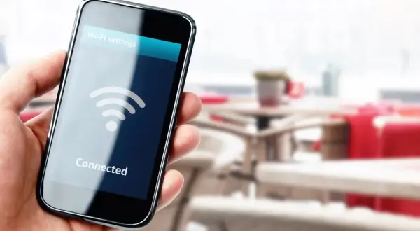 Dłoń trzyma smartfon z napisem "Connected" i ikoną Wi-Fi. W tle widać stoliki kawiarniane.