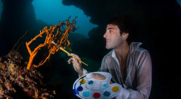 Un artista subacqueo crea foto creative, dipingendo un corallo arancione con una tavolozza colorata.