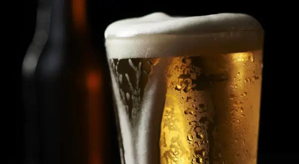 Bicchiere di birra olandese dorata con schiuma bianca e goccioline di condensa, su sfondo scuro.