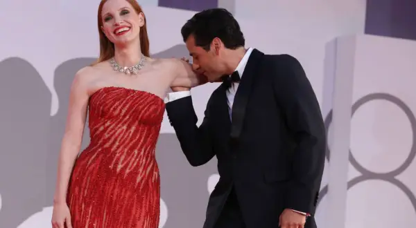 Oscar Isaac besa la mano de Jessica Chastain, quien luce un vestido rojo brillante y un collar de diamantes.