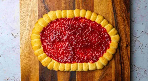 Pyszny mazurek pistacjowy z malinami, ozdobiony delikatnymi ciasteczkami, kusi swoim wyglądem.