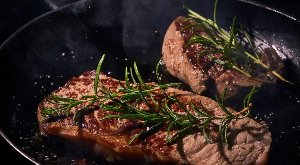 Zwei saftige Rumpsteaks braten in einer Pfanne, garniert mit Rosmarin und grobem Salz. Dampf steigt auf und verheißt ein köstliches Mahl.