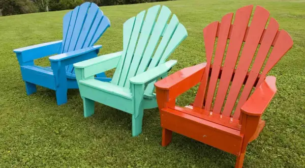 Tres sillas de madera de estilo Adirondack, pintadas de azul, verde menta y naranja, listas para disfrutar del exterior. ¡Pintar sillas de madera sin lijar es fácil!