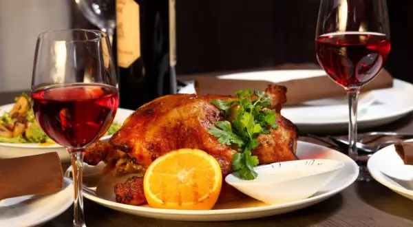 Idealne jakie wino do gęsi? Czerwone wino i pieczona gęś z pomarańczą i ziołami, na elegancko zastawionym stole.