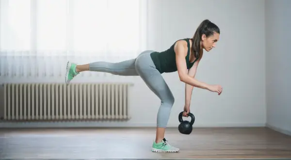 Woman performing kettlebell balance exercises, balancing on one leg while holding a kettlebell.