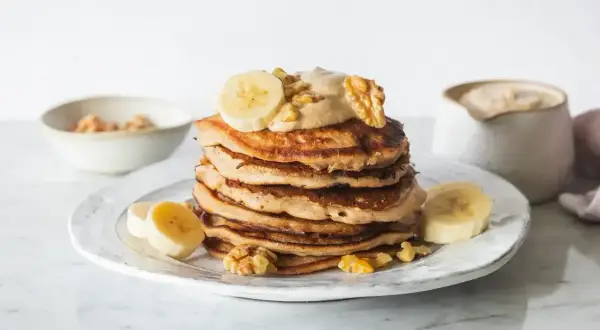 Stos placuszków bananowych z kremem, bananami i orzechami włoskimi na talerzu.