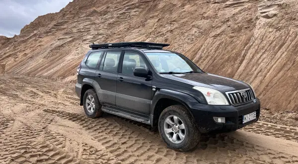 Czarny Land Cruiser 120 na piaszczystym podłożu, z bagażnikiem dachowym, gotowy na terenową przygodę.