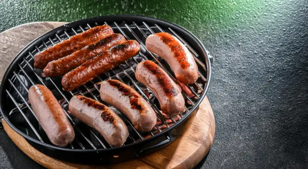 Mehrere rohe Bratwürste braten auf einem Grill. Sie sind noch nicht ganz durch, aber schon schön gebräunt.