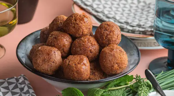 Un piatto pieno di polpette di fagioli dorate, guarnite con erbe fresche.