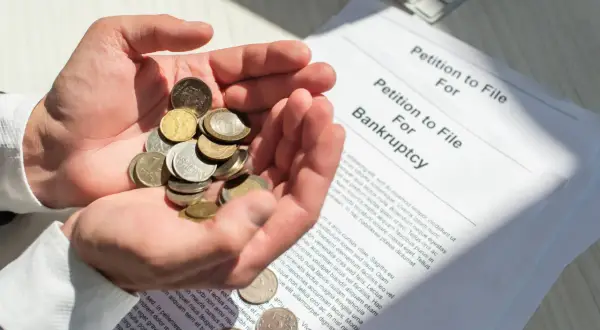 Dłonie trzymają garść monet obok dokumentu "Petition to File For Bankruptcy". To obrazuje, co się dzieje po ogłoszeniu upadłości konsumenckiej.