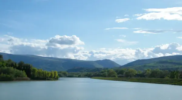 Vasto lago delle grazie con colline verdi e cielo azzurro con nuvole bianche.