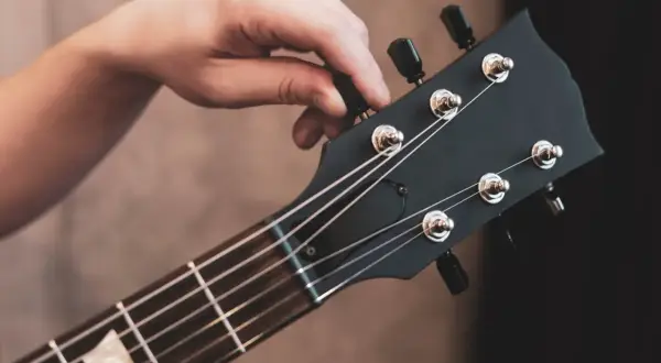 Dłoń kręci kluczem, by nastroić gitarę. Idealne brzmienie czeka!