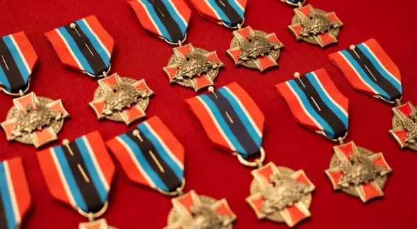 Kolekcja medali i odznaczeń OSP z orłem i czerwono-niebiesko-czarnymi wstążkami, ułożona na czerwonym tle.
