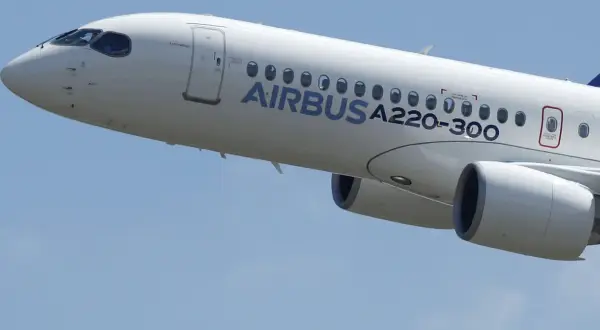 Biały samolot Airbus a220-300 wznosi się na błękitne niebo.