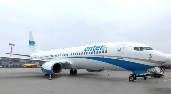 Biały samolot Enter Air z niebieskimi pasami na tle pochmurnego nieba. Gotowy do startu, by zabrać pasażerów w podróż.