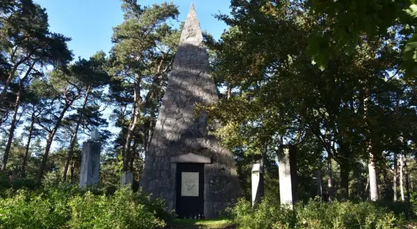 Kamienna piramida Łakińskiego w lesie, otoczona drzewami i zielenią. Obok stoją kamienne pomniki.