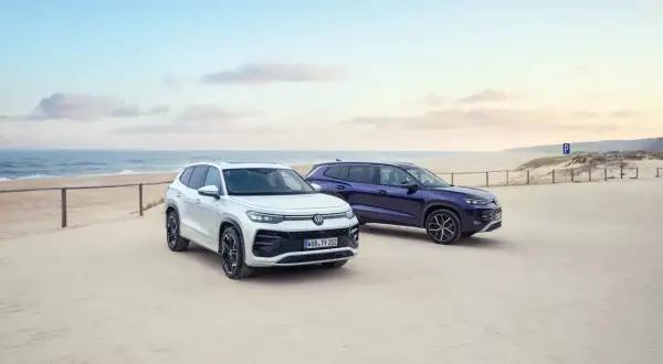 Dwa SUV-y, biały i granatowy, zaparkowane na piaszczystej plaży. To nowe modele VW Tayron, gotowe na przygodę nad morzem.