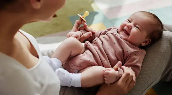 Mama bawi się z dzieckiem, które radośnie gaworzy, trzymając smoczek.