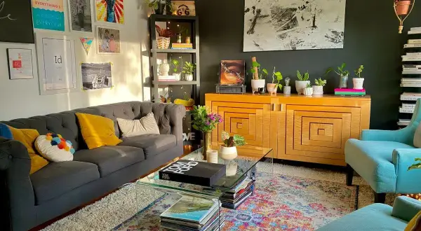 Salon w stylu maksymalistycznym: szara sofa, turkusowe fotele, kolorowy dywan, mnóstwo roślin i dekoracji na ścianach.