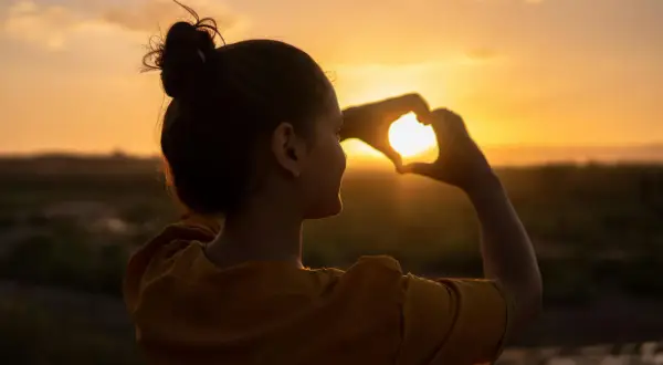 Silueta de mujer haciendo un corazón con las manos al atardecer, reflejando su actitud positiva ante la vida.